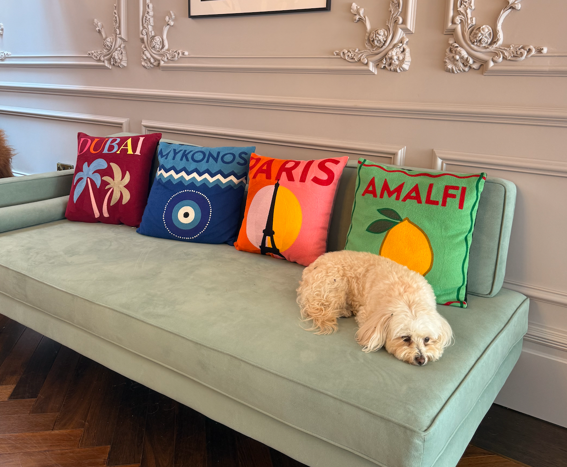 Truffles the dog on a sofa with Dubai, Mykonos, Paris and Amalfi needlepoint cushions