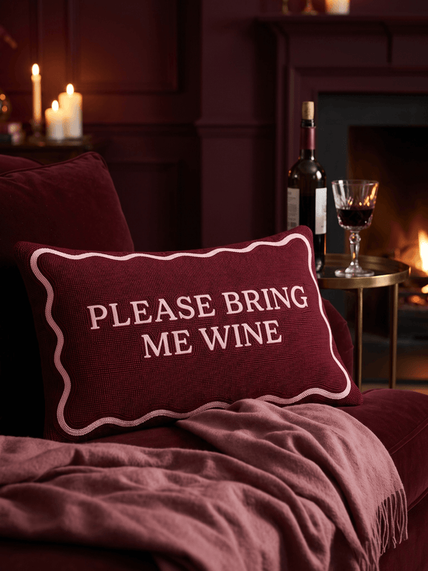 Please Bring Me Wine needlepoint cushion on a burgundy velvet sofa by candlelight